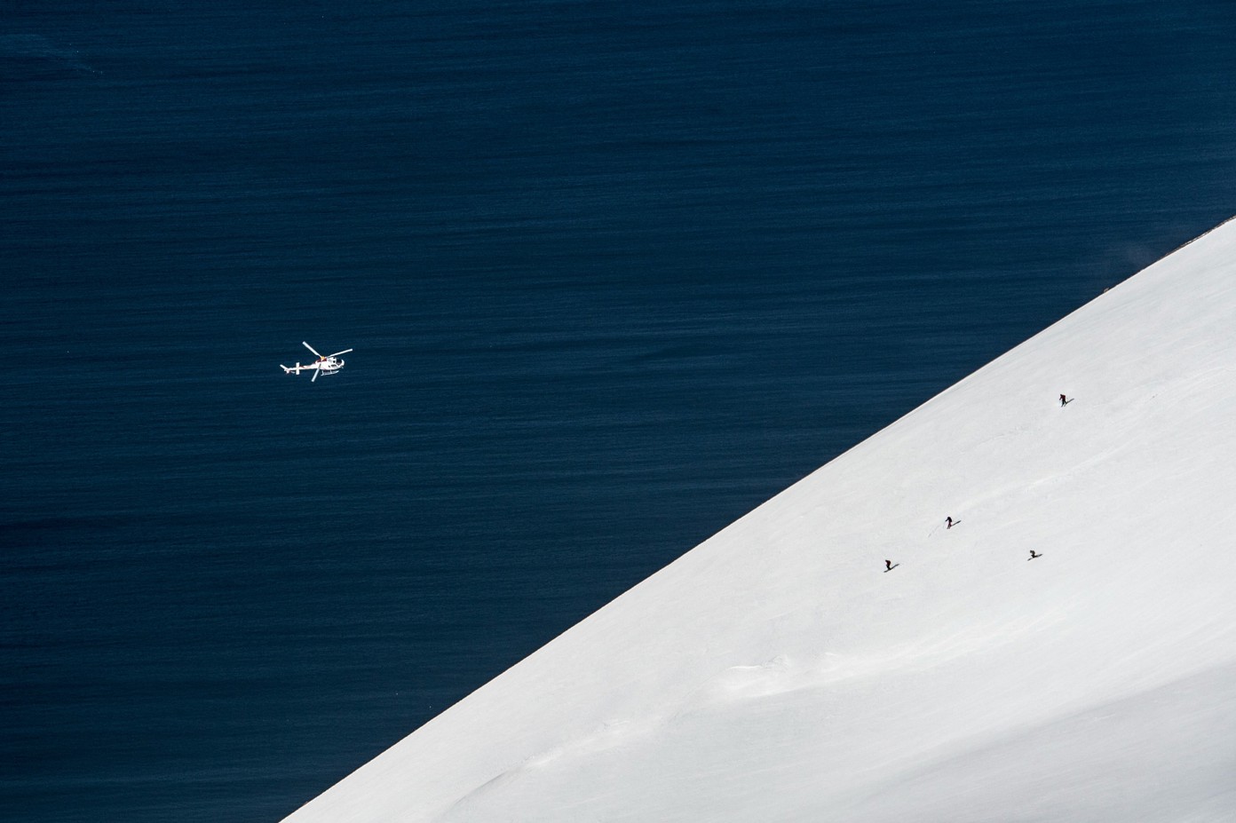 An aerial view of a helicopter flying over head and three skiers.